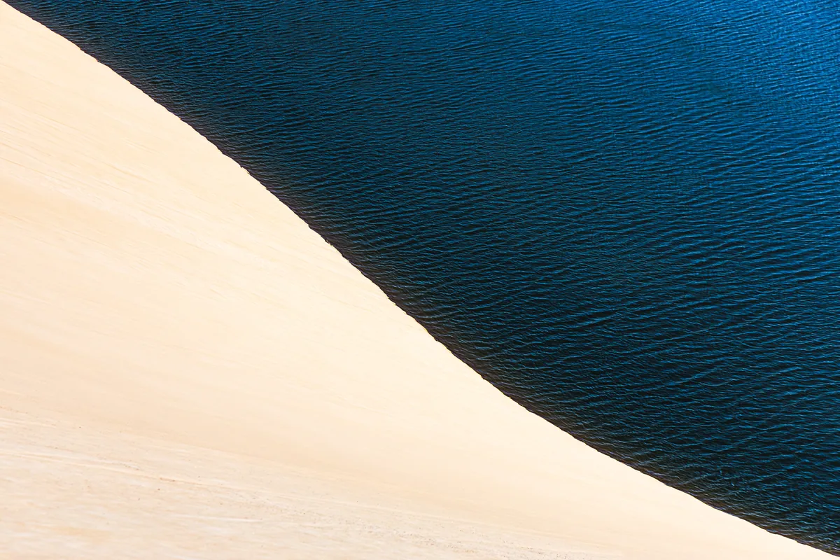 A areia clara encontra a água azul-escura numa composição minimalista.