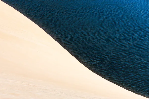 A areia clara encontra a água azul-escura numa composição minimalista.