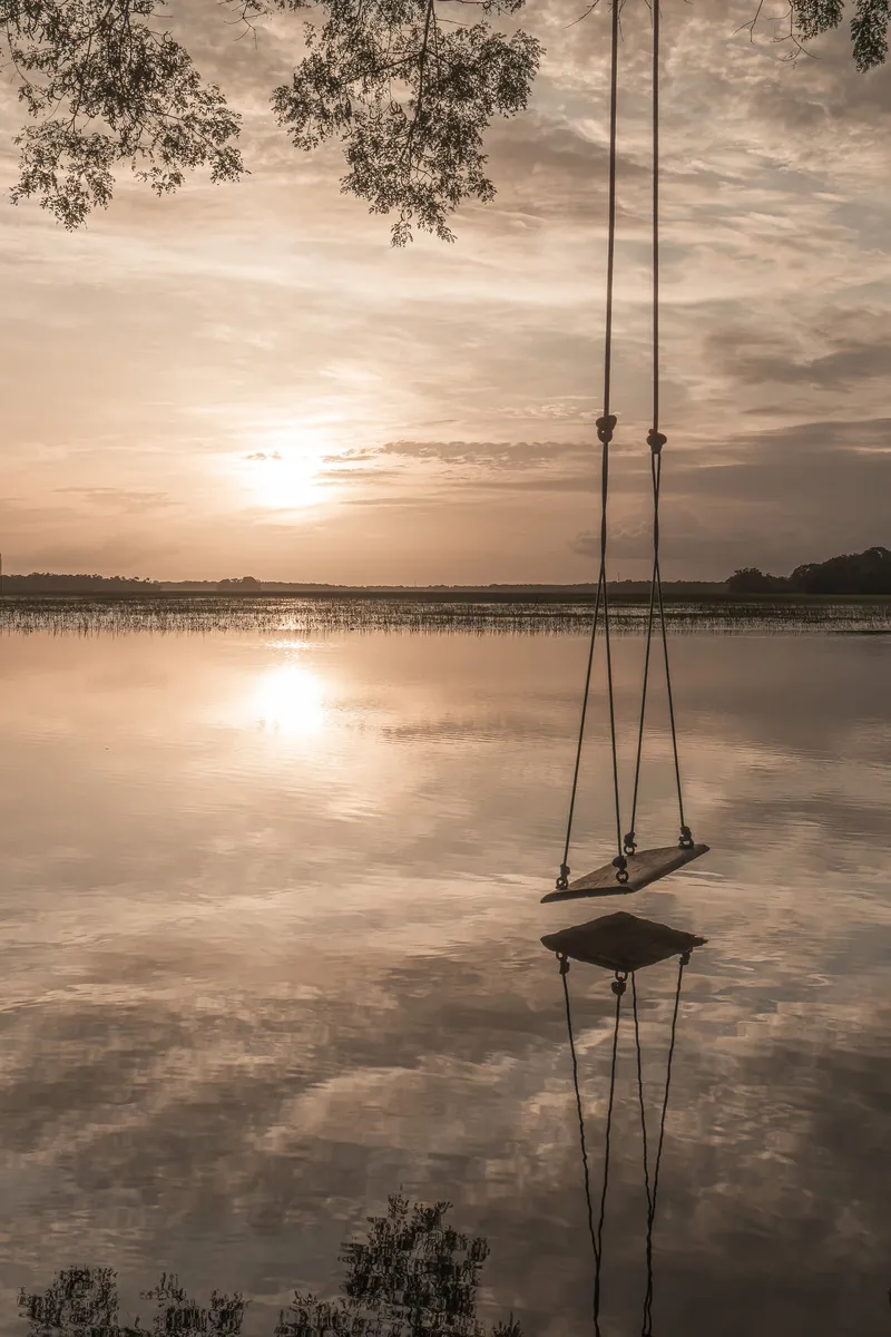 Um balanço suspenso sobre o lago espelhado reflete o céu do entardecer.