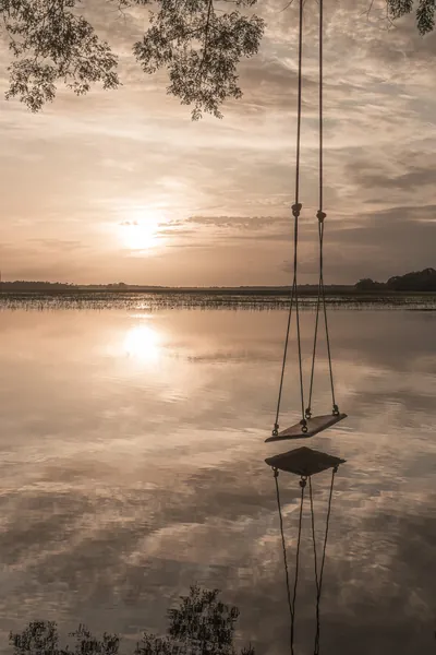Um balanço suspenso sobre o lago espelhado reflete o céu do entardecer.