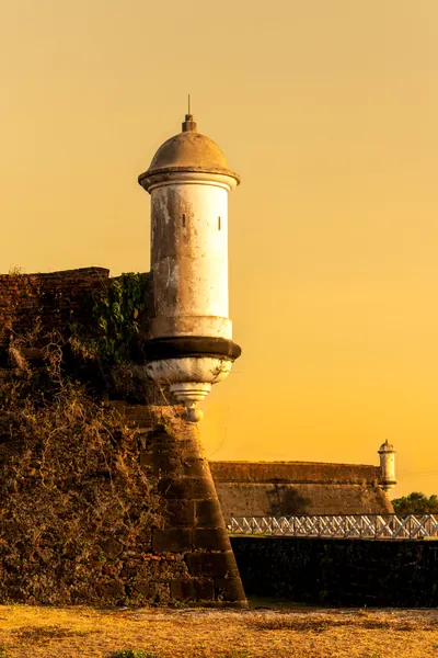 Guarita da Fortaleza recortada contra um céu inteiramente dourado.
