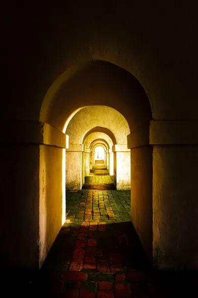 Uma sequência de arcos iluminados forma um túnel de luz quente no interior da Fortaleza.