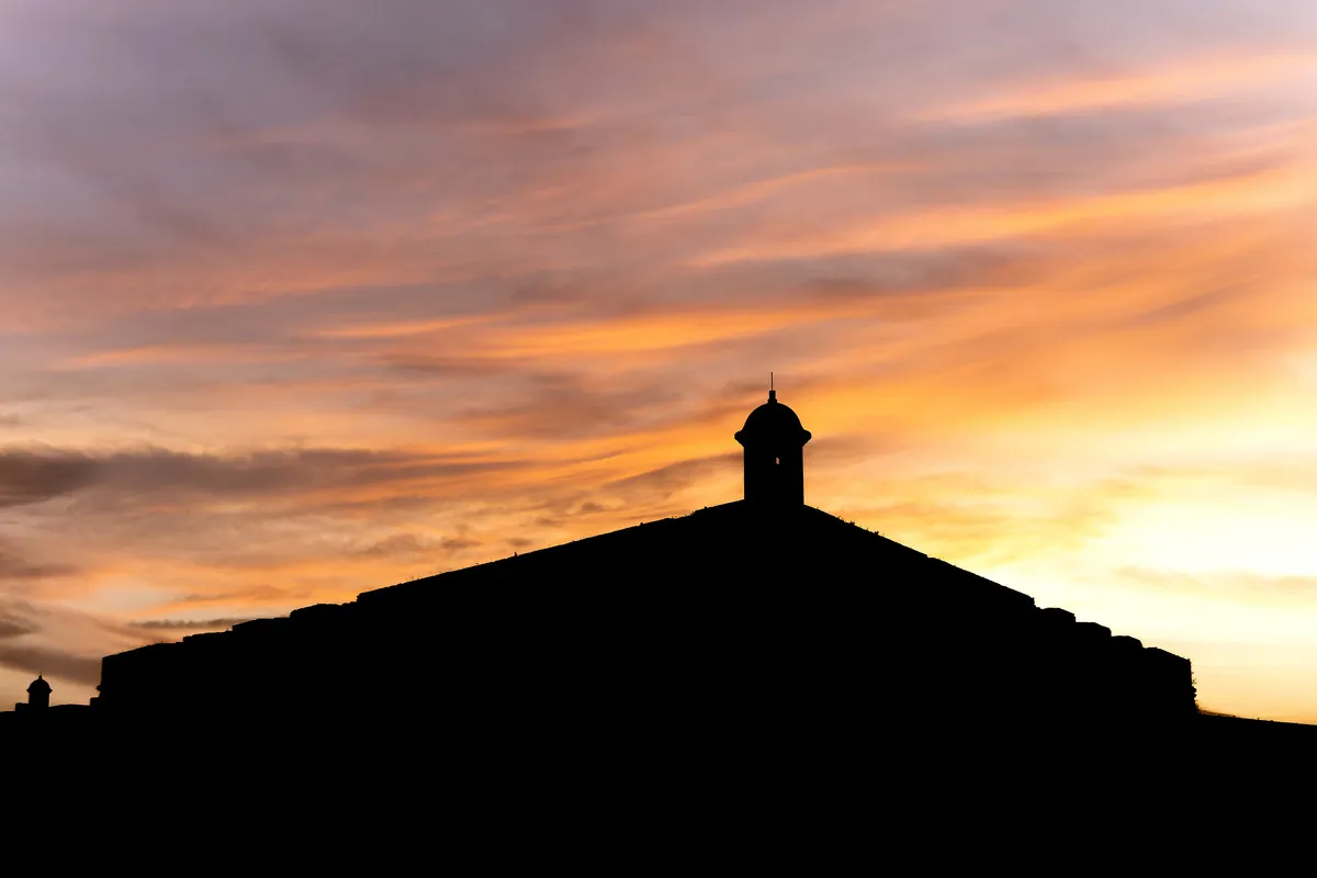Silhueta da Fortaleza e de sua guarita contra o céu em chamas do crepúsculo.