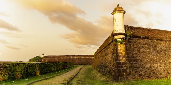 Guarita branca e muralha de pedra da Fortaleza sob o céu dourado do fim de tarde.