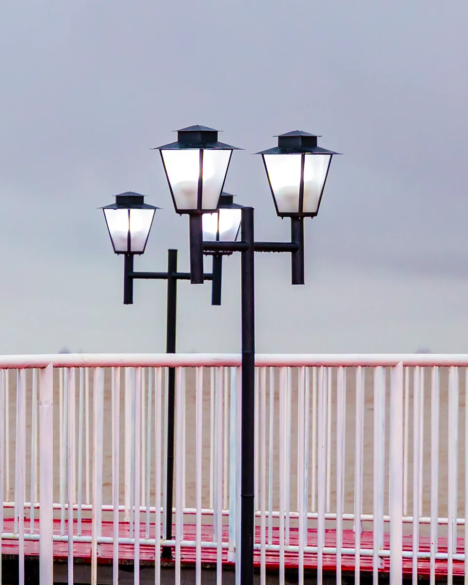 Luminárias clássicas contra o céu cinza, acima do guarda-corpo vermelho e branco.