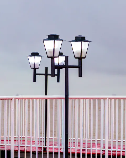 Luminárias clássicas contra o céu cinza, acima do guarda-corpo vermelho e branco.