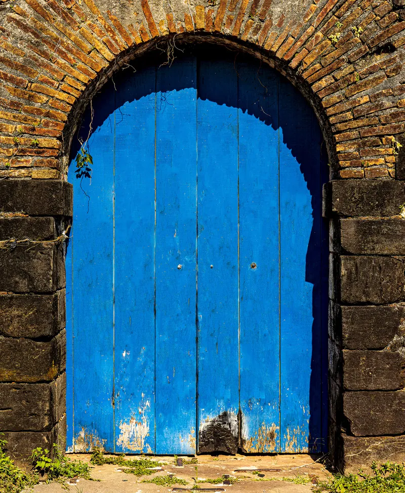 Uma porta azul desgastada sob o arco de tijolos aparentes.